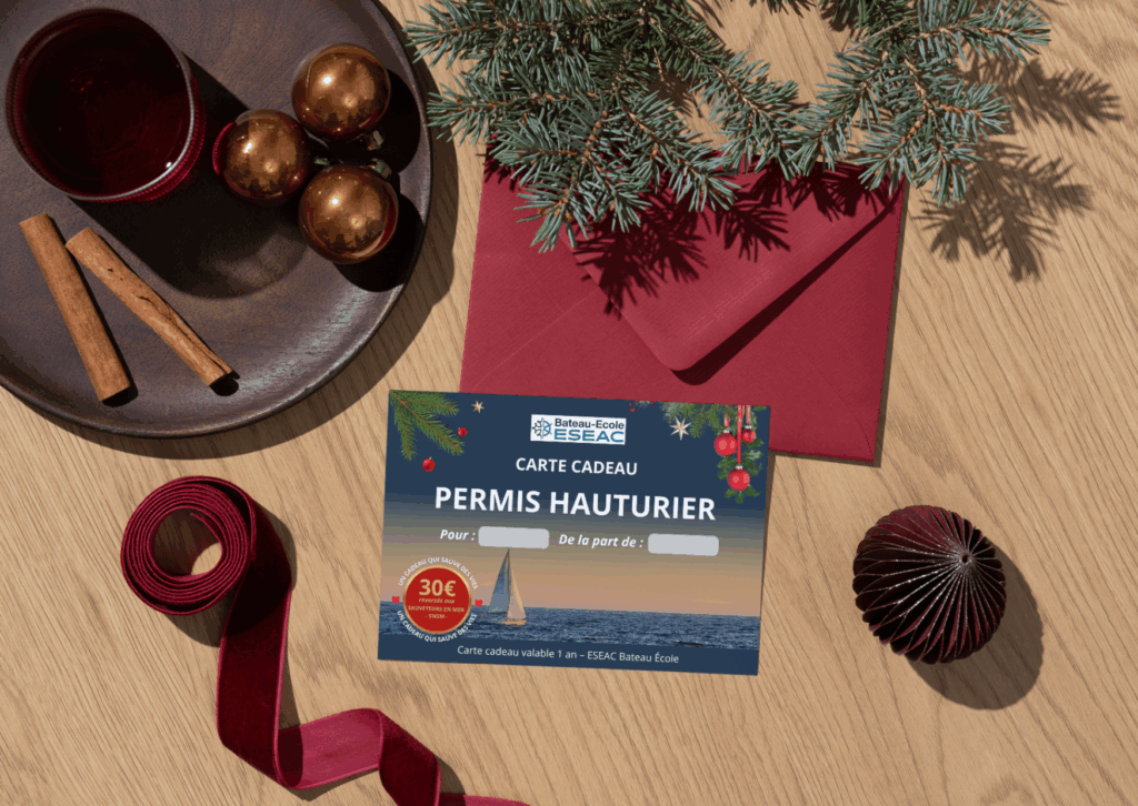 Carte cadeau de Noel 2025 ESEAC Bateau École pour le permis hauturier, posée sur une table en bois décorée de Noël avec des rubans rouges et des bâtons de cannelle. Idée cadeau pour perfectionner sa navigation en mer et prendre le large. Moniteur avec 30 ans d'expérience et bénévole à la SNSM. Pour chaque carte cadeau acheté, un don de 30€ est reversé aux sauveteurs en mer. Un cadeau qui a du sens et qui sauve des vies.